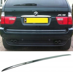 Op de afbeelding: Achteraanzicht van een donkergroene SUV met rode achterlichten, een gele kentekenplaat en dubbele uitlaatpijpen. Een chromen sierlijst wordt onder het voertuig getoond. De SUV heeft de modelnaam "X5" aan de rechterkant.