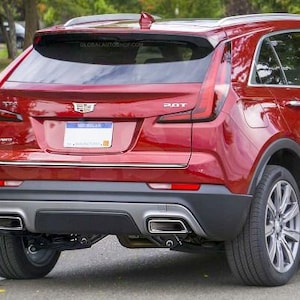Puede incluir: Vista trasera de un SUV Cadillac XT4 rojo. El vehículo tiene molduras cromadas, tubos de escape dobles y una placa de matrícula de Michigan. La imagen muestra las luces traseras, el parachoques trasero y la insignia 2.0T.
