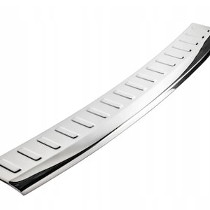 May include: A shiny, silver car door sill protector with a rectangular shape. The protector has a series of recessed rectangular grooves along its length. The surface is highly reflective, creating a bright, metallic appearance.