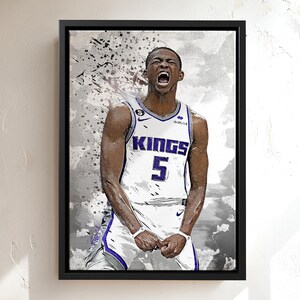 May include: A framed canvas print showing a stylized portrait of a basketball player in a white and purple jersey with the word "KINGS" and the number "5". The artwork has a black frame and a grey and white background with paint splatter effects.