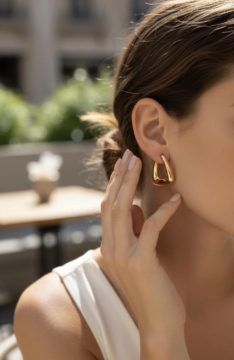 K&ouml;nnte beinhalten: Goldfarbene, tropfenf&ouml;rmige Ohrringe. Die Ohrringe haben eine glatte, polierte Oberfl&auml;che und einen hohlen Innenraum. Das Design ist eine einfache, elegante Tropfenform. Die Ohrringe werden am Ohr getragen.