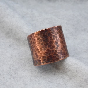 May include: A wide copper ring with a hammered texture. The ring is a warm copper color and has a slightly irregular shape.