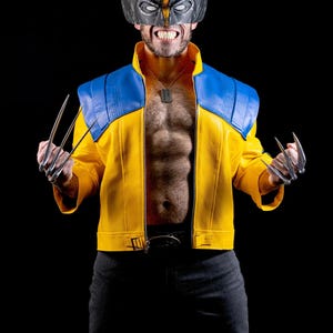 Könnte beinhalten: Eine gelb-blaue Jacke mit hohem Kragen, getragen zu einer schwarzen Hose. Das Outfit umfasst eine gelb-schwarze Maske mit spitzen Ohren, eine silberne Erkennungsmarken-Halskette und metallische Klauenaufsätze an den Händen als Kostüm.
