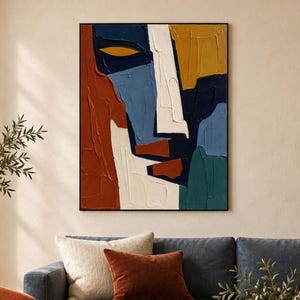 Può includere: Un'opera d'arte murale rettangolare raffigurante un volto astratto composto da spesse pennellate materiche nei toni del blu profondo, arancione bruciato, giallo senape e crema, incorniciata da un sottile bordo nero con finitura a impasto.
