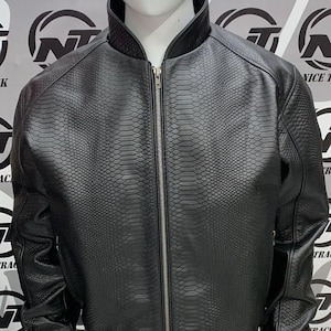 May include: Black faux leather bomber jacket with a snakeskin texture, a zip-up front, and a ribbed collar and cuffs. The jacket is displayed on a mannequin. The background features the text "NICE TRACK" and a logo.