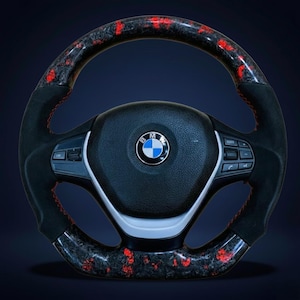 May include: A black and red carbon fiber steering wheel with a BMW logo in the center. The wheel has red stitching and control buttons. The rim has a black and red pattern.