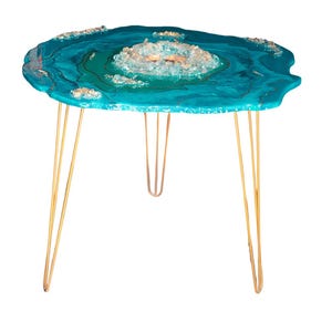 Könnte beinhalten: Ein runder Beistelltisch mit einer türkisfarbenen Epoxidharzplatte, die ein zentrales kristallines Design und goldene Akzente aufweist. Der Tisch hat goldene Haarnadelbeine und schafft eine moderne und künstlerische Ästhetik. Der Tisch hat einen Durchmesser von ca. 61 cm.