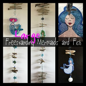 May include: A set of three large, freestanding mermaid and fish embroidery designs. The designs are blue, green, and pink and are embroidered on a white fabric. The designs are attached to a string of driftwood.