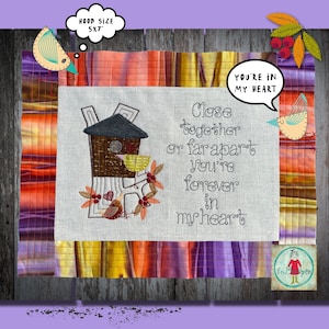 Könnte beinhalten: Stickerei auf einem beigefarbenen Stoff mit einem Vogelhaus, Vögeln und dem Text "Close together or far apart you're forever in my heart". Der Stoff ist von einem bunten Patchwork aus Stoff umgeben.
