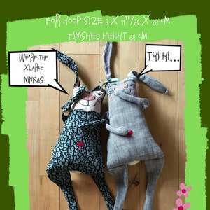 Puede incluir: Dos peluches de conejo de tela gris y azul con caras bordadas y el texto "We're the XLarge Ninkas" y "Thi Hi..." en bocadillos de diálogo. Los peluches están tumbados sobre una superficie de madera con flores bordadas de color rosa.