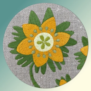 May include: A close-up of a yellow embroidered flower with green leaves on a linen fabric background.