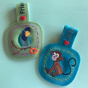 May include: Two embroidered felt keychains, one green with a blue bird and the word "Frie" and the other blue with a monkey and the word "Frie".