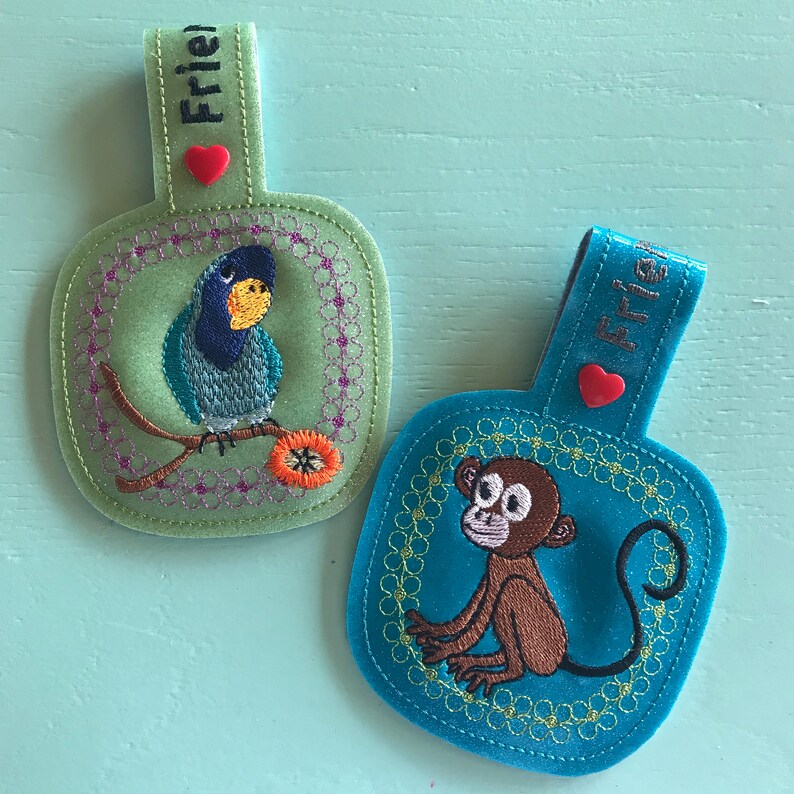 May include: Two embroidered felt keychains, one green with a blue bird and the word "Frie" and the other blue with a monkey and the word "Frie".