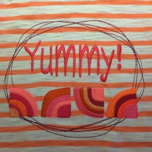 Könnte beinhalten: Ein weiß-orangenes gestreiftes Shirt mit dem Wort "Yummy!" in rot gestickt. Das Shirt hat außerdem vier gestickte regenbogenfarbene Bögen.
