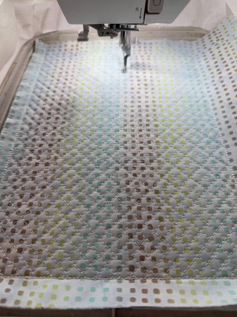 Puede incluir: Primer plano de una tela blanca con un patr&oacute;n repetitivo de peque&ntilde;os puntos verdes, azules y marrones. La tela se est&aacute; cosiendo en una m&aacute;quina de coser.