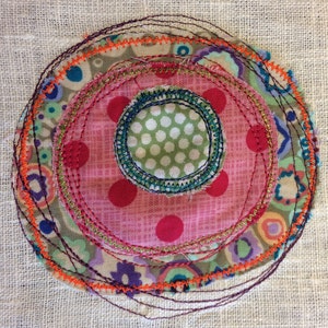 Könnte beinhalten: Ein bunter Stoffkreis mit mehreren Schichten von Nähten. Der mittlere Kreis ist grün mit weißen Punkten, umgeben von einem rosa Kreis mit roten Punkten und dann einer Schicht aus Blumenstoff.