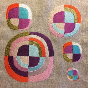 May include: Five embroidered circles with geometric patterns in shades of pink, purple, orange, teal, and gold on a beige linen background.