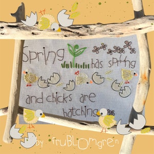 May include: A white fabric with embroidery depicting a spring scene with chicks hatching from eggs. The text reads "Spring has sprung and chicks are hatching" with the signature "by fruBLOMgren" at the bottom.
