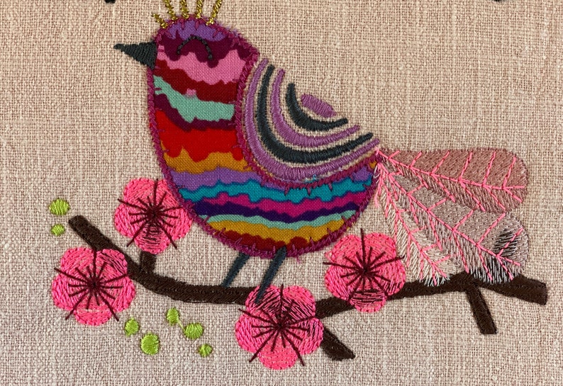 May include: Embroidered design of a colorful bird with a crown perched on a branch with pink flowers. The bird has a striped body with a purple, pink, red, orange, yellow, green, and blue pattern.