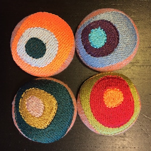 May include: Four round fabric ornaments with embroidered concentric circles in various colors, including orange, blue, green, yellow, red, and pink.
