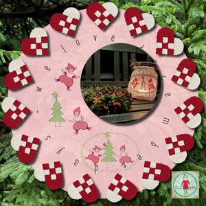 May include: A pink wreath with red and white hearts, each with a woven pattern. The wreath is decorated with the words "We love December" and features illustrations of elves and Christmas trees.