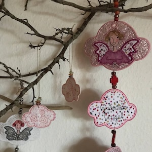 May include: Pink and white felt ornaments with embroidered angels and clouds. The ornaments are hanging from a branch with string and beads. One ornament has the text "Guardian Angel" on it.