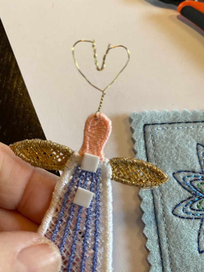 Puede incluir: Un adorno de &aacute;ngel hecho a mano con cabeza rosa, vestido a rayas azul y blanco, alas dor&eacute;es y halo de coraz&oacute;n de alambre.
