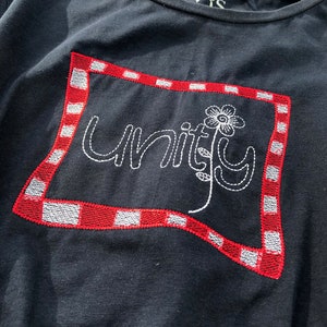 Könnte beinhalten: Schwarzes T-Shirt mit rot-weiß kariertem, gesticktem Rand. Das Wort "unity" ist in weißer Schrift innerhalb des Randes gestickt, begleitet von einem weißen Blumendesign. Das T-Shirt hat einen Rundhalsausschnitt.