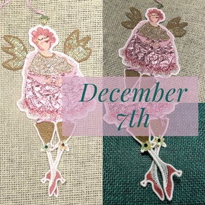 Könnte beinhalten: Ein rosa-goldener Engel-Anhänger mit glitzerndem Kleid und Flügeln. Der Anhänger hängt an einer Schnur und trägt den Text "December 7th".