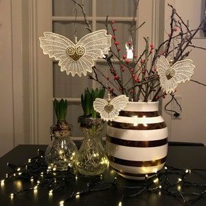 May include: A white vase with brown stripes holds a branch with white lace butterfly ornaments and red berries. Two clear glass vases with hyacinths are in the foreground. A string of white lights is on the table.