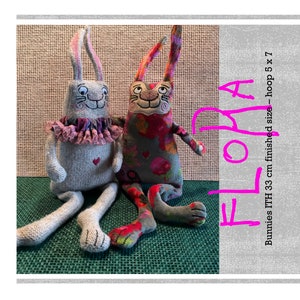 Op de afbeelding: Twee pluche konijnen speelgoed, een grijs met roze versiering en een met een bloemenpatroon, zittend op een groene ondergrond. De tekst "ELORA" is in roze op een grijze achtergrond geschreven. De tekst "Bunnies 1TH 33 cm finished size - hoop 5 x 7" is ook op de grijze achtergrond geschreven.