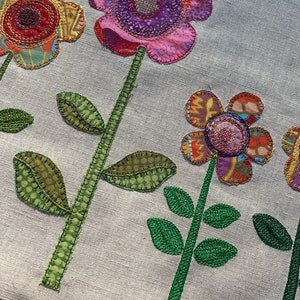 Puede incluir: Una tela blanca con cinco flores bordadas. Las flores est&aacute;n hechas de telas de diferentes colores y tienen una variedad de patrones. Las flores son todas de diferentes tama&ntilde;os y formas. La tela es de color beige claro.