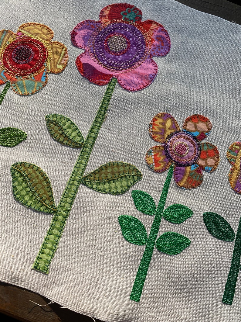 Puede incluir: Una tela blanca con cinco flores bordadas. Las flores est&aacute;n hechas de telas de diferentes colores y tienen una variedad de patrones. Las flores son todas de diferentes tama&ntilde;os y formas. La tela es de color beige claro.