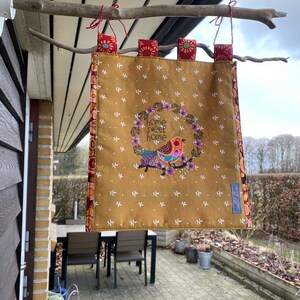 May include: A yellow fabric banner with a bird and floral wreath design. The banner has the text "home sweet home" embroidered on it. The banner is hanging from a branch.