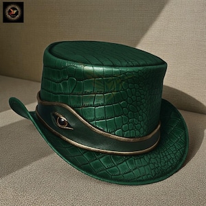 Op de afbeelding: Een groene hoge hoed met een krokodillenleertextuur. De hoed heeft een brede rand en een band met een oogvormig detail. De hoed heeft een vintage, steampunk esthetiek.