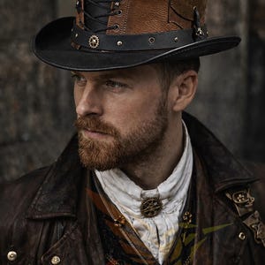 May include: A top hat featuring a black crown and brim with a brown leather side panel, black lace-up detailing, and a black leather hat band adorned with small metallic gear accents and studs. The hat has a structured, flat-top silhouette.
