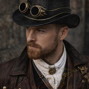 May include: Black steampunk-style hat with attached goggles. The hat features a textured pattern and a wide brim. The goggles have gold-colored frames. The hat is part of a steampunk-themed outfit, with a brown leather jacket and a white collared shirt.