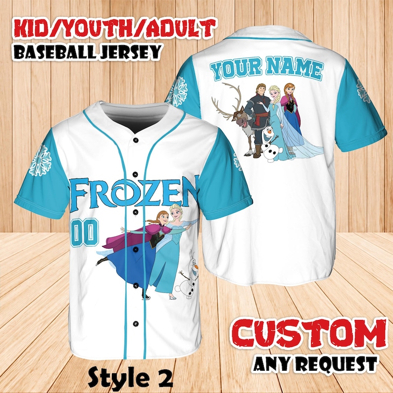 Puede incluir: Camiseta de b&eacute;isbol blanca con mangas y detalles en azul claro. La parte delantera presenta la palabra "FROZEN" y el n&uacute;mero "00", junto con im&aacute;genes de personajes. La parte trasera tiene el texto "YOUR NAME" y m&aacute;s im&aacute;genes de personajes. La camiseta est&aacute; etiquetada como "Style 2".