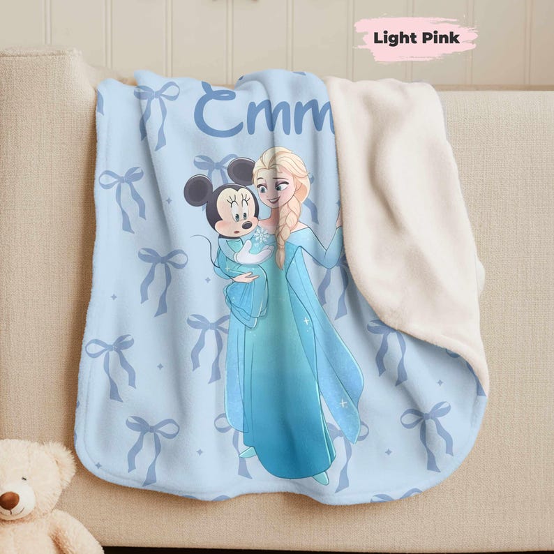 Puede incluir: Manta azul claro con un patr&oacute;n de lazos y el nombre "Emm". Presenta personajes de Disney, Elsa y Mickey Mouse. El reverso es de material suave color crema. Adecuada para la cama de un ni&ntilde;o o un sof&aacute;.