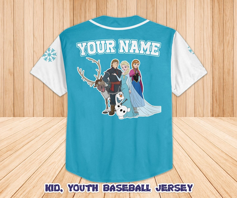 Puede incluir: Una camiseta de b&eacute;isbol azul claro con mangas y cuello blancos. La parte trasera presenta un gr&aacute;fico de personajes de dibujos animados y el texto "YOUR NAME". El texto "KID, YOUTH BASEBALL JERSEY" est&aacute; en la parte inferior.