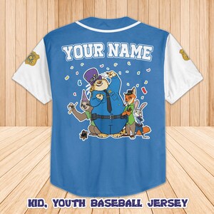 Peut inclure: Un maillot de baseball bleu avec des manches blanches et un col blanc. Le maillot pr&eacute;sente une illustration de personnages de Zootopie. Le texte "YOUR NAME" est au-dessus de l'illustration. Le texte "KID, YOUTH BASEBALL JERSEY" est en bas.