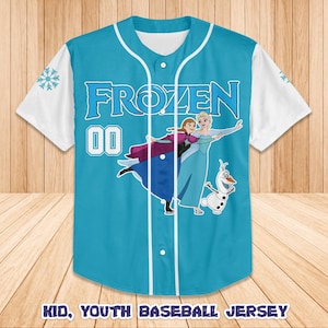Puede incluir: Una camiseta de b&eacute;isbol azul claro con la palabra "FROZEN" en blanco y el n&uacute;mero "00". La camiseta tiene mangas blancas y un gr&aacute;fico de personajes de la pel&iacute;cula Frozen. El texto "KID, YOUTH BASEBALL JERSEY" est&aacute; en la parte inferior.