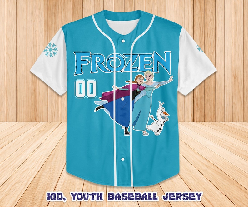 Puede incluir: Una camiseta de b&eacute;isbol azul claro con la palabra "FROZEN" en blanco y el n&uacute;mero "00". La camiseta tiene mangas blancas y un gr&aacute;fico de personajes de la pel&iacute;cula Frozen. El texto "KID, YOUTH BASEBALL JERSEY" est&aacute; en la parte inferior.