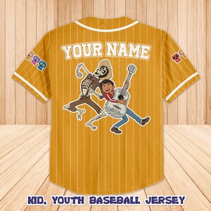 Peut inclure: Maillot de baseball jaune moutarde pour jeunes avec des fines rayures blanches, un col et des bordures de manches blancs. Comporte un graphisme d'un squelette et d'un gar&ccedil;on jouant de la guitare. Le texte "YOUR NAME" est au-dessus du graphisme.