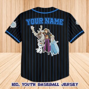 Puede incluir: Camiseta de b&eacute;isbol negra con rayas azules y ribetes. Presenta el texto "YOUR NAME" en azul en la espalda, junto con un gr&aacute;fico de personajes de la pel&iacute;cula Frozen. La parte inferior de la camiseta dice "KID, YOUTH BASEBALL JERSEY".