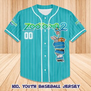 Op de afbeelding: Een turquoise honkbalshirt met witte krijtstrepen, met de tekst "Zootopia 2" en het nummer "00". Het shirt heeft een cartoonafbeelding van personages uit de film. De tekst "Kid, Youth Baseball Jersey" staat onderaan.