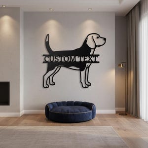 Puede incluir: Arte de pared de metal negro que representa un perro con el texto "CUSTOM TEXT". El perro está de perfil, con una cola larga y orejas puntiagudas. Debajo de la obra de arte hay una cama para perros azul marino.
