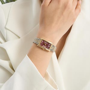 Könnte beinhalten: Eine gold-silberne Armbanduhr mit rechteckigem, weinrotem Zifferblatt und römischen Ziffern. Die Uhr hat ein zweifarbiges Metallarmband. Die Person trägt einen weißen Blazer. Die Uhr wird am Handgelenk getragen.