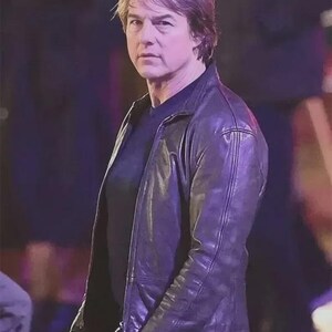 May include: A person wearing a dark purple leather jacket over a black shirt and blue jeans. The jacket has a classic design with a front zipper and a tailored fit. The person is looking directly at the camera.