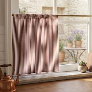 Peut inclure: Un rideau de type vitrage à rayures verticales rouge foncé et blanches est suspendu à une fine tringle en laiton fixée à l'intérieur du cadre de la fenêtre. Le tissu est froncé en haut, créant des plis souples tombant sur le rebord.
